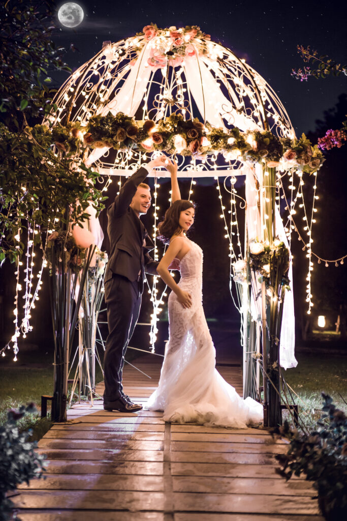 Full length of wedding couple dancing in illuminated gazebo at night
